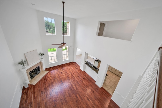 living area featuring hardwood / wood-style floors, a ceiling fan, a high ceiling, and a glass covered fireplace