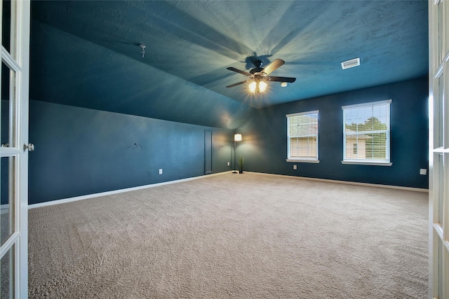 empty room featuring carpet, vaulted ceiling, ceiling fan, baseboards, and visible vents