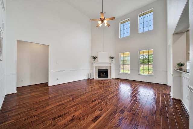 unfurnished living room with a towering ceiling, ceiling fan, wood finished floors, and a tile fireplace