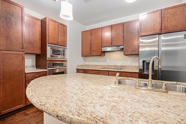 kitchen featuring a sink, stainless steel appliances, under cabinet range hood, light stone counters, and dark wood finished floors