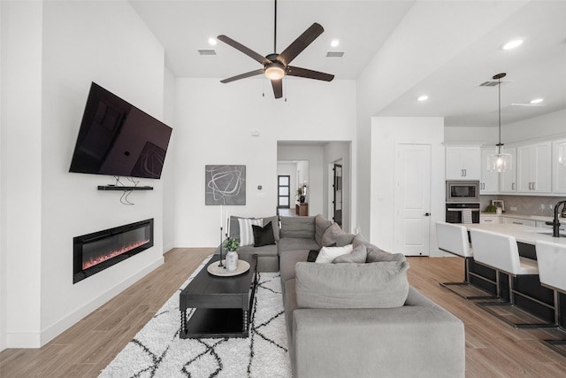 4623 Bridgewood Dr, Spring, TX 77386 - living room featuring high vaulted ceiling, a ceiling fan, a glass covered fireplace, light wood-style floors, and baseboards