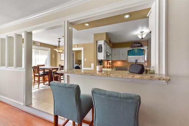 kitchen featuring decorative backsplash, light stone counters, a peninsula, washer / dryer, and white cabinetry