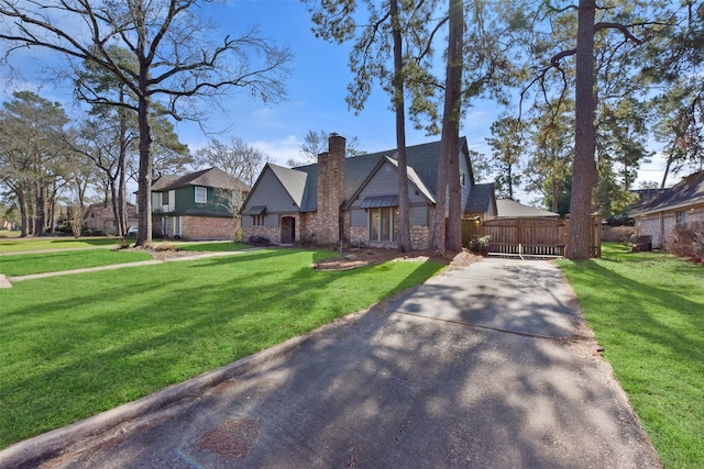 tudor house featuring a front lawn, aphalt driveway, fence, a chimney, and brick siding