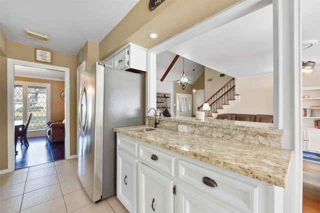 kitchen with visible vents, a sink, light stone counters, freestanding refrigerator, and white cabinetry