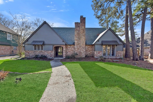 english style home featuring brick siding, a chimney, a shingled roof, and a front lawn