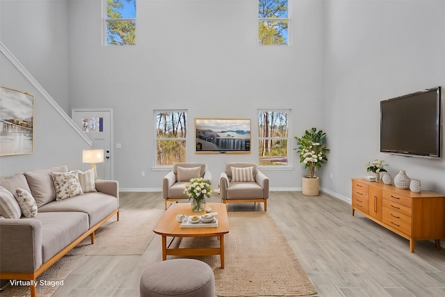 living area with a towering ceiling, light wood finished floors, and a healthy amount of sunlight