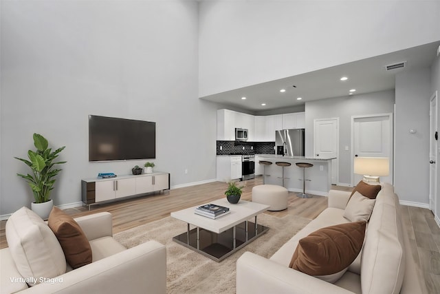 living area with recessed lighting, light wood finished floors, baseboards, visible vents, and a high ceiling