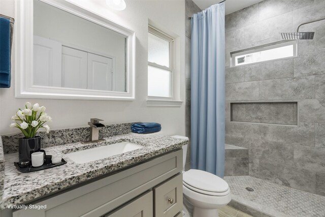 bathroom featuring toilet, a tile shower, vanity, and plenty of natural light