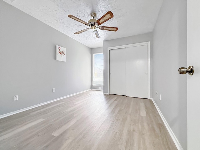 unfurnished bedroom featuring a textured ceiling, a closet, light wood-style flooring, and baseboards