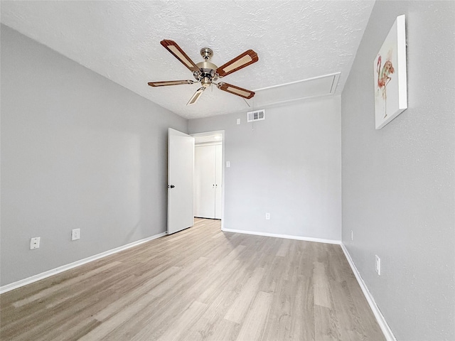 spare room featuring attic access, a ceiling fan, visible vents, a textured ceiling, and wood finished floors