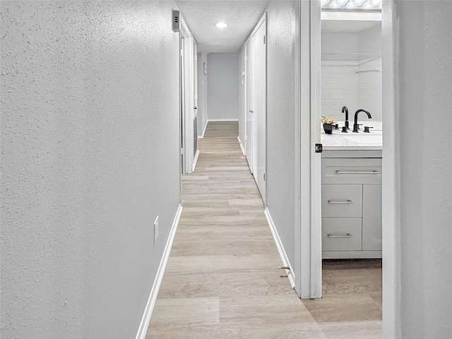 hall featuring light wood finished floors, a textured wall, and baseboards