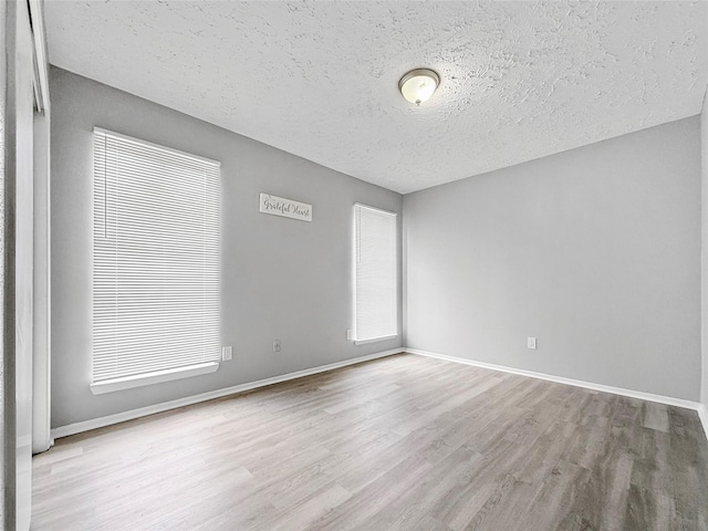 unfurnished room with a textured ceiling, wood finished floors, and baseboards
