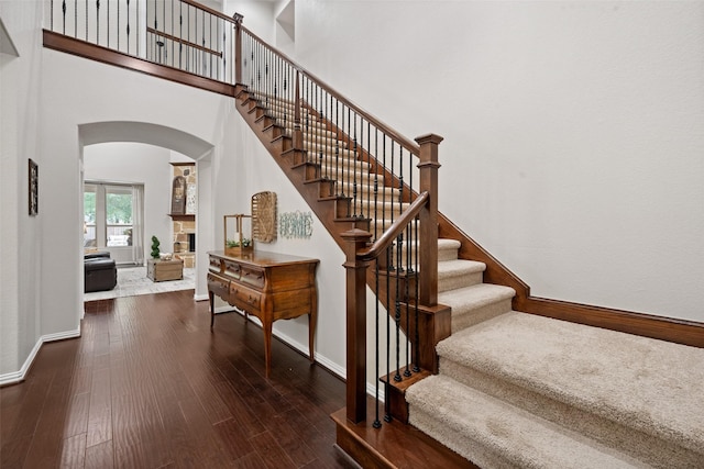 stairway with a fireplace, wood finished floors, baseboards, and arched walkways