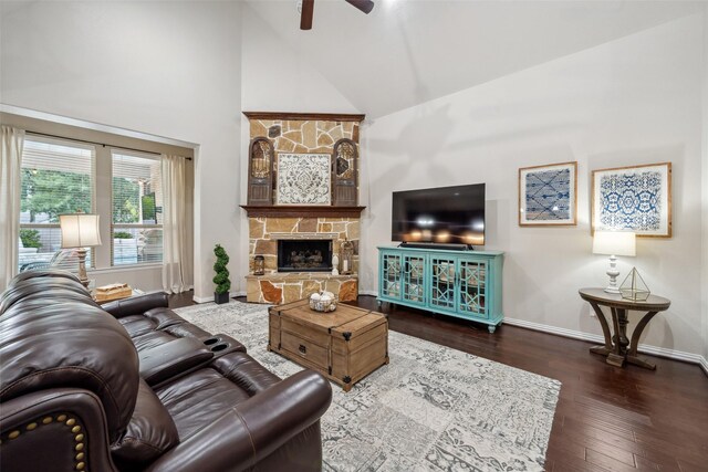 living room with ceiling fan, baseboards, wood finished floors, high vaulted ceiling, and a stone fireplace