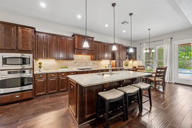 kitchen with light stone counters, a breakfast bar area, stainless steel appliances, a sink, and visible vents