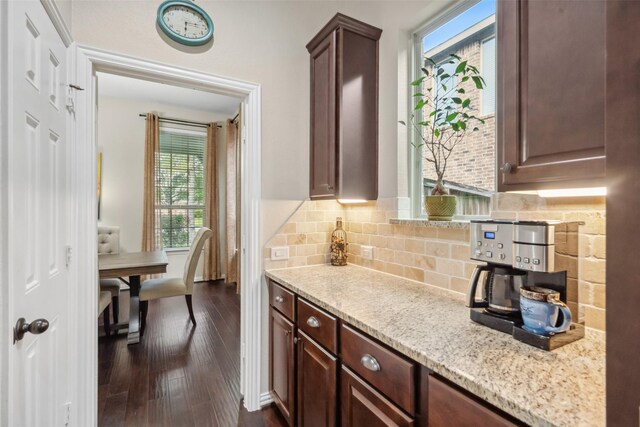 kitchen with light stone countertops, dark wood-style flooring, dark brown cabinets, and tasteful backsplash