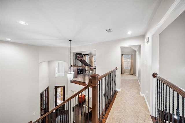 hallway featuring an upstairs landing, visible vents, carpet flooring, and arched walkways