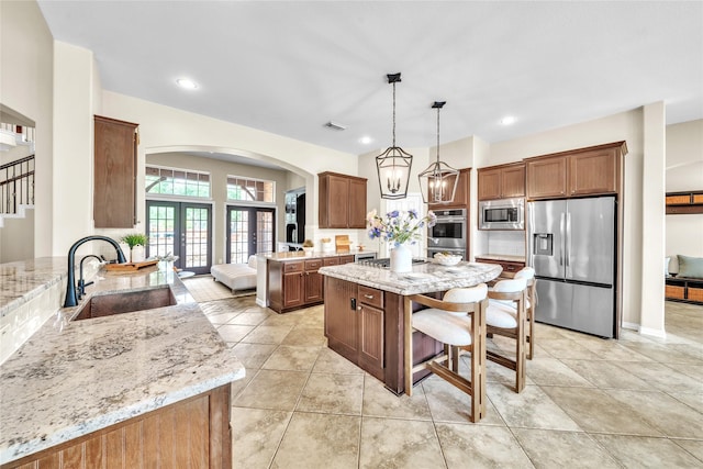 kitchen with light stone counters, a sink, arched walkways, and stainless steel appliances