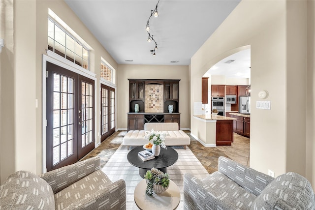 living area featuring french doors, visible vents, arched walkways, rail lighting, and baseboards