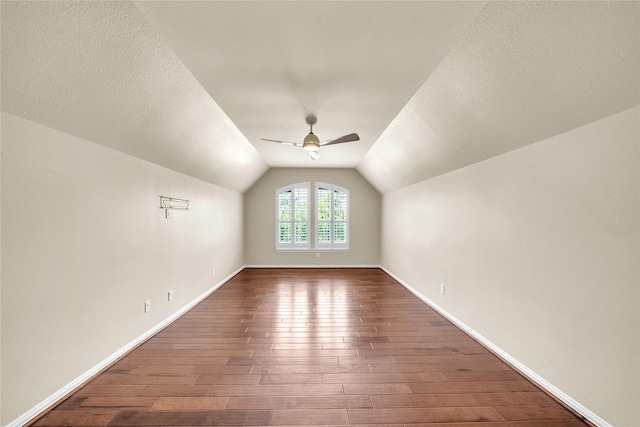 additional living space featuring dark wood-style flooring, ceiling fan, vaulted ceiling, and baseboards