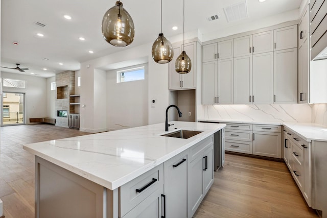 4705 Gibson St, Houston, TX 77007 - kitchen with a sink, light stone counters, light wood-style flooring, backsplash, and a kitchen island with sink