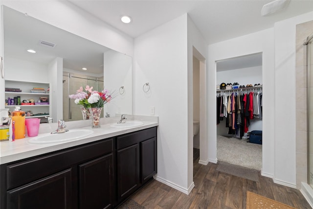 full bath with a walk in closet, a shower stall, double vanity, and a sink