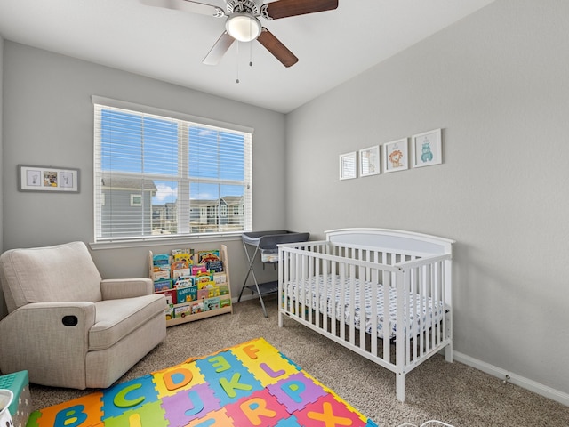 carpeted bedroom featuring a nursery area, baseboards, multiple windows, and a ceiling fan