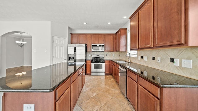 kitchen with tasteful backsplash, appliances with stainless steel finishes, a kitchen island, a sink, and a notable chandelier