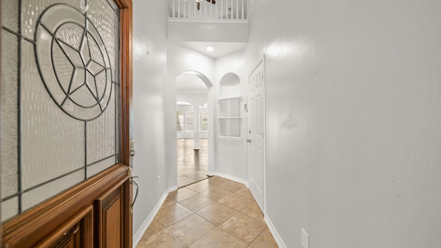 interior space featuring baseboards, light tile patterned floors, arched walkways, and a high ceiling