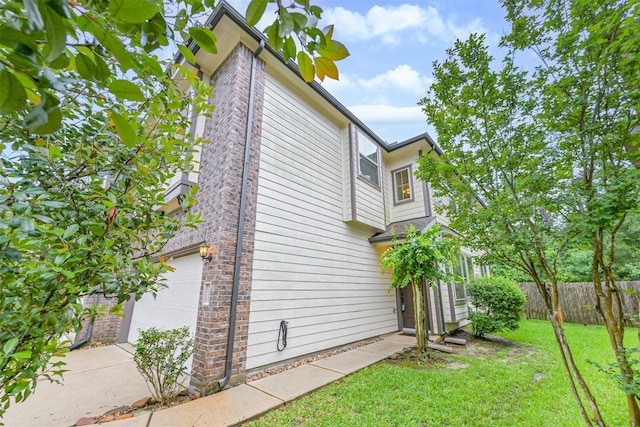 view of property exterior with an attached garage, fence, concrete driveway, and a lawn