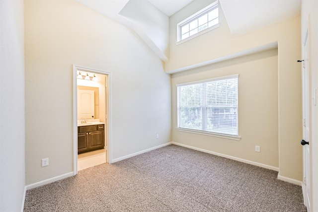 unfurnished bedroom with baseboards, a high ceiling, light colored carpet, and a sink
