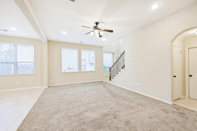 unfurnished living room with light colored carpet, baseboards, arched walkways, recessed lighting, and a ceiling fan