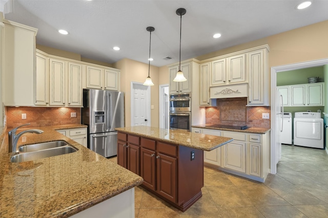 kitchen featuring light stone counters, a sink, a center island, stainless steel appliances, and washing machine and dryer