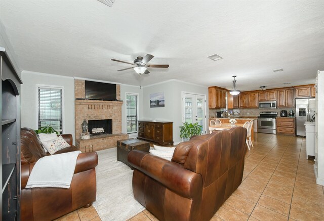living area featuring light tile patterned floors, ornamental molding, ceiling fan, a brick fireplace, and visible vents
