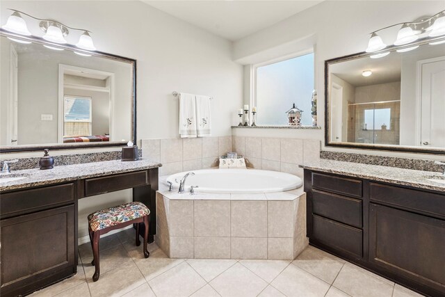 ensuite bathroom featuring two vanities, a bath, tile patterned flooring, and a stall shower