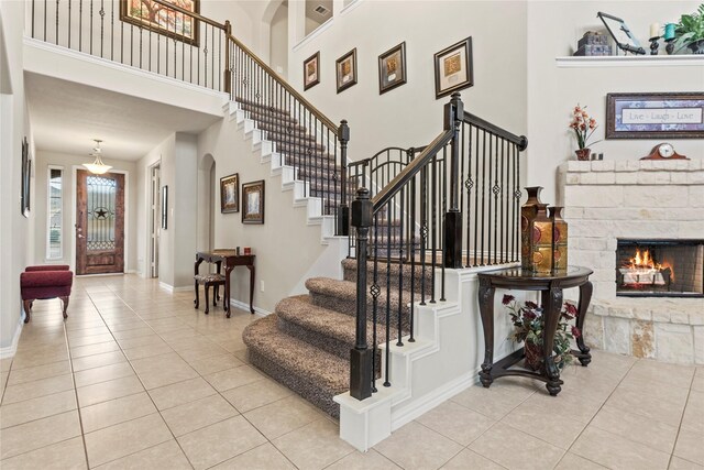 staircase featuring a fireplace, baseboards, tile patterned flooring, and a high ceiling