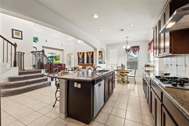 kitchen featuring range hood, a sink, stainless steel appliances, a breakfast bar area, and arched walkways