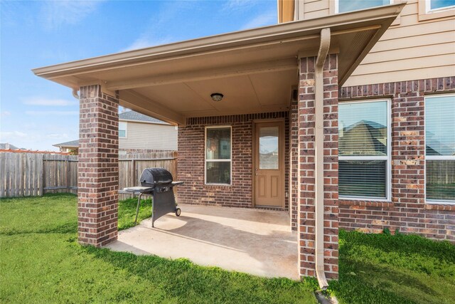entrance to property featuring brick siding, fence, a yard, and a patio area