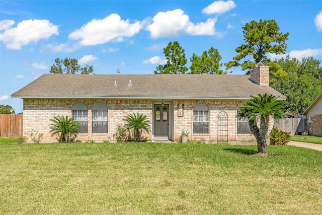 ranch-style home featuring a chimney, brick siding, fence, roof with shingles, and a front yard