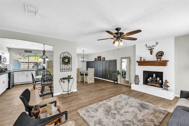 living room featuring a textured ceiling, visible vents, light wood-type flooring, and ceiling fan with notable chandelier