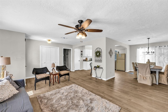living room with arched walkways, ceiling fan with notable chandelier, light wood finished floors, baseboards, and a textured ceiling