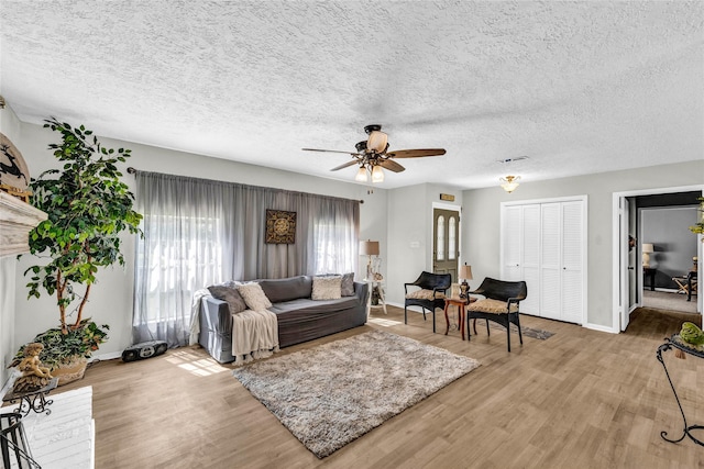 living area with baseboards, ceiling fan, a textured ceiling, and light wood finished floors