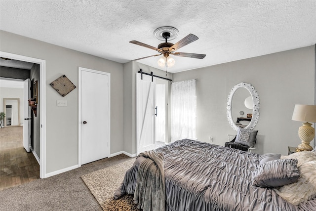 bedroom with a barn door, carpet, baseboards, a ceiling fan, and a textured ceiling