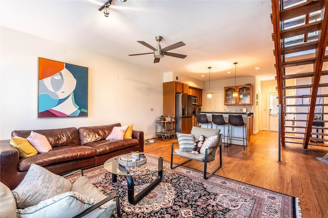 living room featuring rail lighting, light wood-style floors, ceiling fan, and baseboards