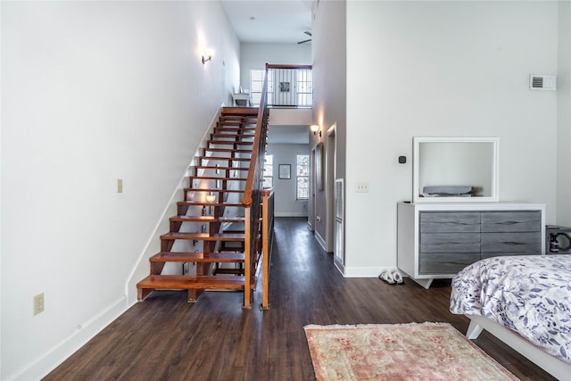 stairway featuring wood finished floors, baseboards, visible vents, and a high ceiling