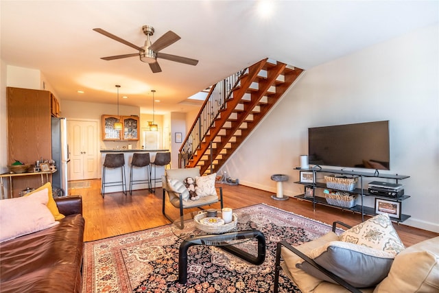 living room with light wood finished floors, stairs, ceiling fan, and baseboards