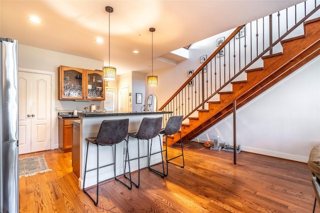kitchen with glass insert cabinets, a kitchen island, dark countertops, a kitchen bar, and light wood finished floors