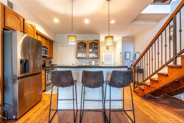 kitchen featuring appliances with stainless steel finishes, a breakfast bar, dark countertops, visible vents, and light wood-type flooring