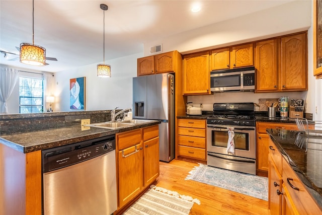 kitchen with brown cabinetry, stainless steel appliances, a sink, visible vents, and pendant lighting