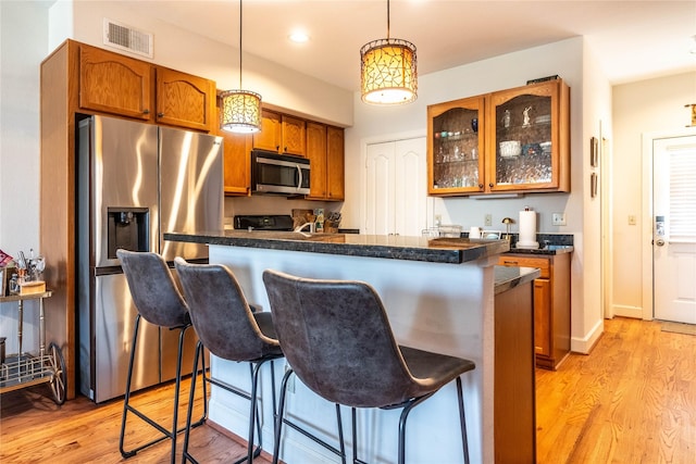 kitchen featuring visible vents, stainless steel appliances, light wood-style floors, and a kitchen breakfast bar